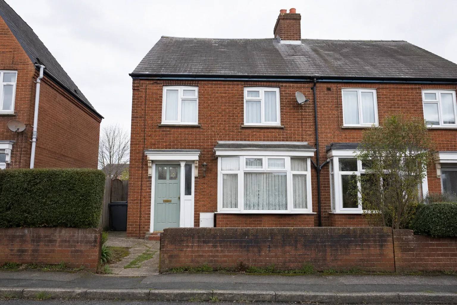 Two-storey brick house photographed square-on from the opposite pavement on an overcast morning